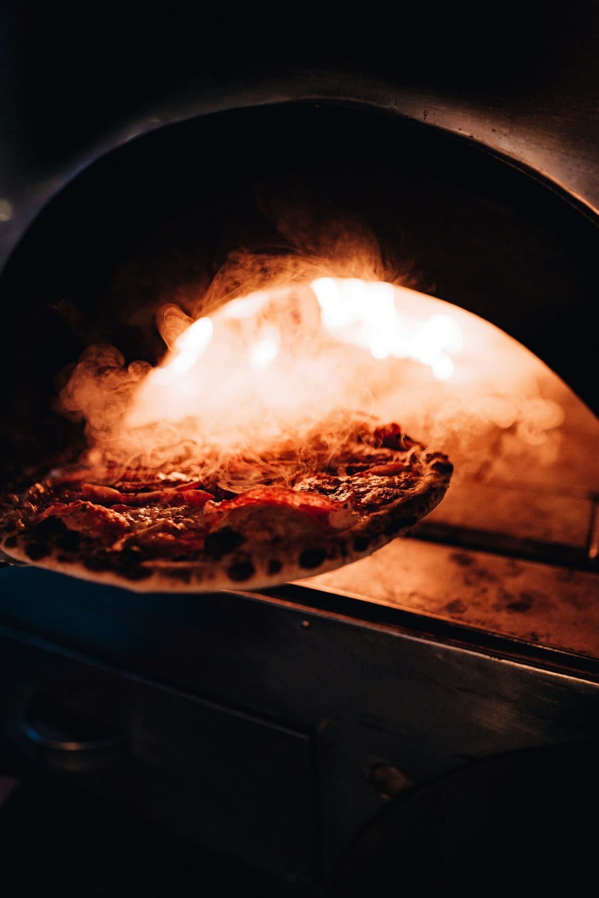 Pizza qui sort du four à bois, encore fumante.